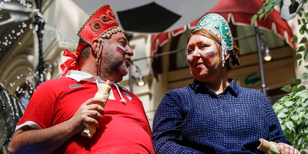 eine Frau und ein Mann mit traditionellem Kopfschmuck, die russische Fahnen auf die Backen geschminkt haben eine Frau und ein Mann mit traditionellem Kopfschmuck, die russische Fahnen auf die Backen geschminkt haben