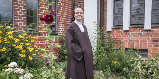 Maria Burger steht in einem Garten vor einem Gebäude aus roten Backsteinen. Maria Burger steht in einem Garten vor einem Gebäude aus roten Backsteinen.