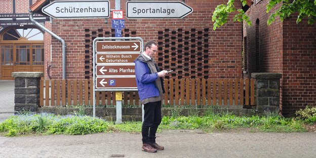 Gerhard Henschel steht vor mehreren Wegweisern. Gerhard Henschel steht vor mehreren Wegweisern.