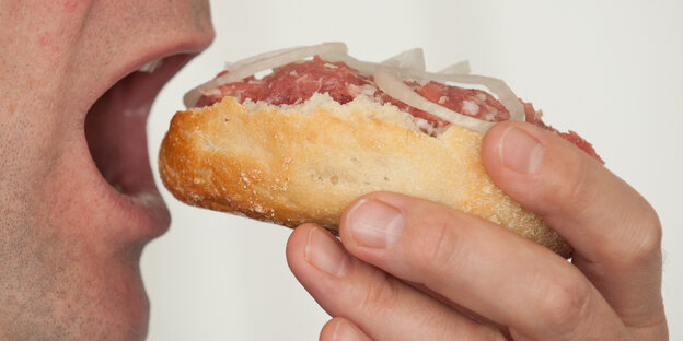 Ein Mann hÀlt ein Mettbrötchen in der Hand und schiebt es sich in den Mund Ein Mann hÀlt ein Mettbrötchen in der Hand und schiebt es sich in den Mund