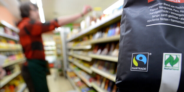 ein verschwommenes Supermarktregal, im Vordergrund eine Tüte mir Fairtrade-Siegel ein verschwommenes Supermarktregal, im Vordergrund eine Tüte mir Fairtrade-Siegel
