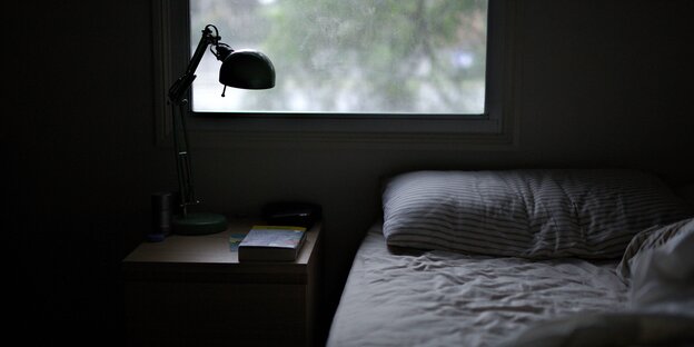 Ein Bett und ein Nachttisch mit Lampe vor einem Fenster. Ein Bett und ein Nachttisch mit Lampe vor einem Fenster.