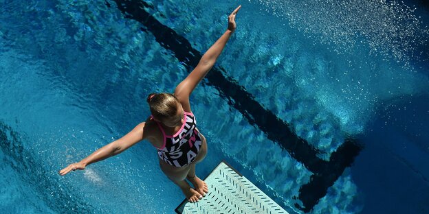 Eine junge Frau steht rückwärts auf einem Sprungturm, unter ihr ein Schwimmbecken Eine junge Frau steht rückwärts auf einem Sprungturm, unter ihr ein Schwimmbecken