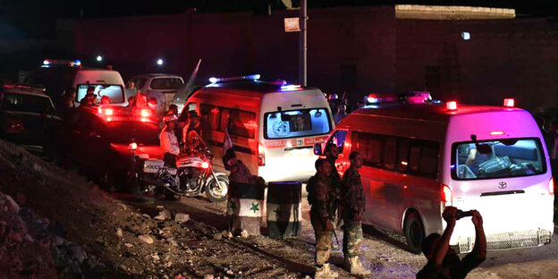 Mehrere Krankenwagen mit Alarmlicht, daneben stehen Personen Mehrere Krankenwagen mit Alarmlicht, daneben stehen Personen