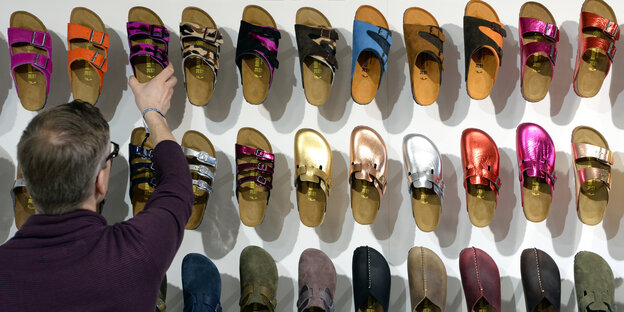 Viele Birkenstockschuhe hängen an einer Wand, ein Mitarbeiter steht davor Viele Birkenstockschuhe hängen an einer Wand, ein Mitarbeiter steht davor
