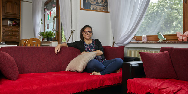 Eine Frau sitzt auf einem roten Sofa und guckt in die Kamera Eine Frau sitzt auf einem roten Sofa und guckt in die Kamera