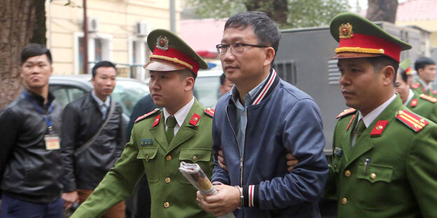 Zwei Vietnamesen in Polizeiuniform führen einen Mann in Handschellen zwischen sich Zwei Vietnamesen in Polizeiuniform führen einen Mann in Handschellen zwischen sich