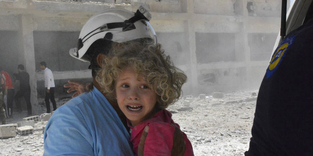 Einer der Weißhelme trägt ein Kind nach einem Luftangriff in Syrien Einer der Weißhelme trägt ein Kind nach einem Luftangriff in Syrien