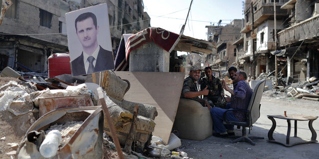Soldaten sitzen an einem selbstgebauten Unterstand, vor dem ein Porträt von Assad aufgestellt ist Soldaten sitzen an einem selbstgebauten Unterstand, vor dem ein Porträt von Assad aufgestellt ist