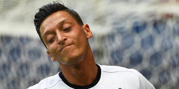 Mesut Özil steht auf dem Platz, lächelt und hat dabei die Augen geschlossen Mesut Özil steht auf dem Platz, lächelt und hat dabei die Augen geschlossen