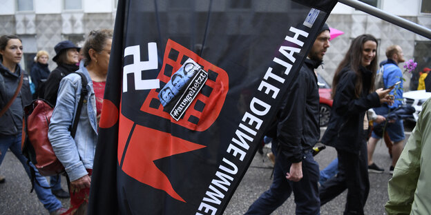 Demonstranten tragen eine Fahne. Darauf eine Figur, die ein Hakenkreuz in einen Mülleimer wirft Demonstranten tragen eine Fahne. Darauf eine Figur, die ein Hakenkreuz in einen Mülleimer wirft
