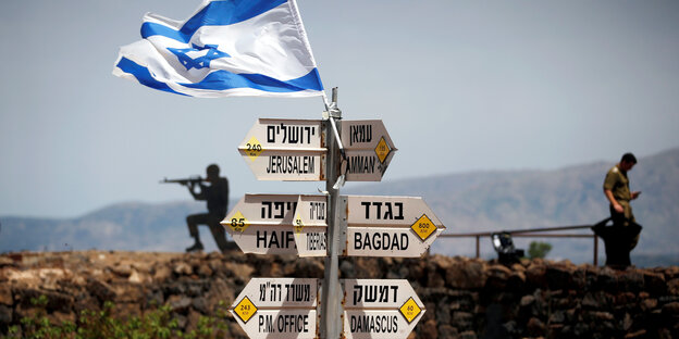 Straßenschilder in einer kargen Gegend, mit einer Israel-Fahne drauf - im Hintergrund israelische Soldaten Straßenschilder in einer kargen Gegend, mit einer Israel-Fahne drauf - im Hintergrund israelische Soldaten