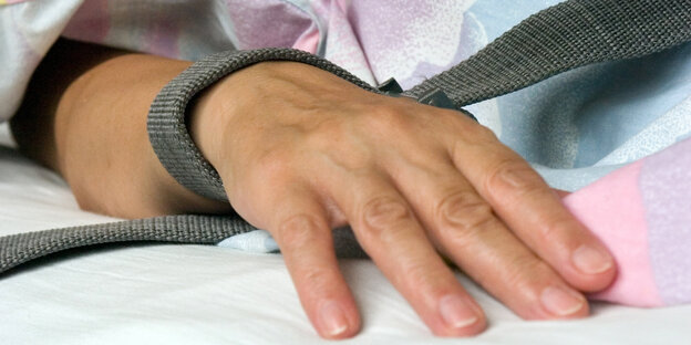 ine mit einem Textilband festgebundene Hand eines Patienten ine mit einem Textilband festgebundene Hand eines Patienten