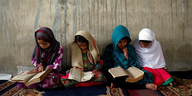 Vier afghanische Mädchen sitzen im Schneidersitz auf dem Teppich und lesen in Büchern