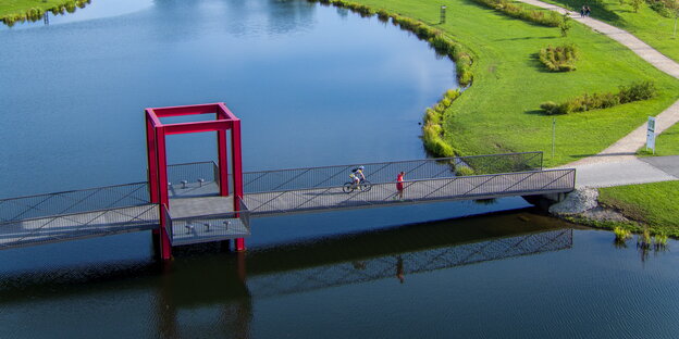 Eine Brücke für Radfahrerinnen für über einen idylischen See Eine Brücke für Radfahrerinnen für über einen idylischen See