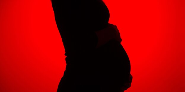 Die schwarze Silouette einer schwangern Person vor rotem Hintergrund Die schwarze Silouette einer schwangern Person vor rotem Hintergrund