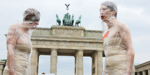 Zwei in Folie eingewickelte Frauen stehen sich vor dem Brandenburger Tor gegenüber Zwei in Folie eingewickelte Frauen stehen sich vor dem Brandenburger Tor gegenüber