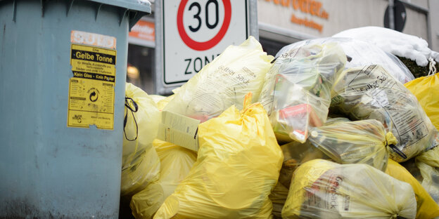 Gelbe Säcke neben einer Plastikmülltonne