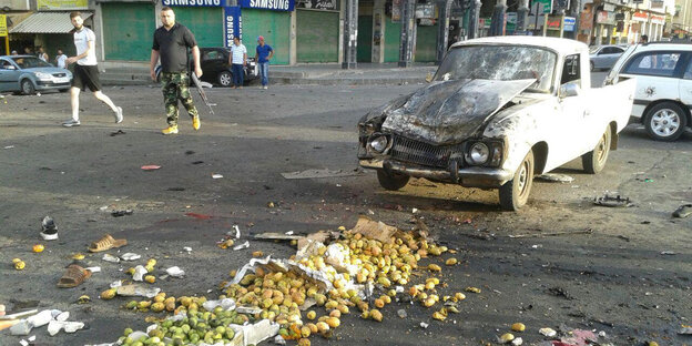 Zwei erschreckte Menschen blicken auf einen halbverkohlten Lieferwafen, Obst liegt verstreut auf der Straße Zwei erschreckte Menschen blicken auf einen halbverkohlten Lieferwafen, Obst liegt verstreut auf der Straße