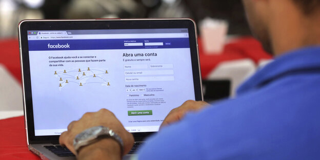 Ein Mann sitzt vor einem Laptop und hat die Seite von Facebook aufgereufen Ein Mann sitzt vor einem Laptop und hat die Seite von Facebook aufgereufen