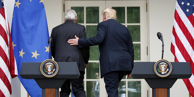 Jean-Claude Juncker und Donald Trump wenden sich von zwei Stehpulten weg, Trump legt Juncker die Hand auf den Rücken Jean-Claude Juncker und Donald Trump wenden sich von zwei Stehpulten weg, Trump legt Juncker die Hand auf den Rücken