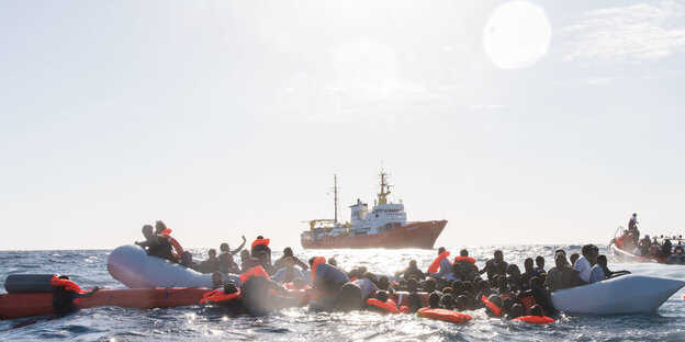 Geflüchtete auf und neben einem Schlauchboot. Einige tragen Rettungswesten Geflüchtete auf und neben einem Schlauchboot. Einige tragen Rettungswesten