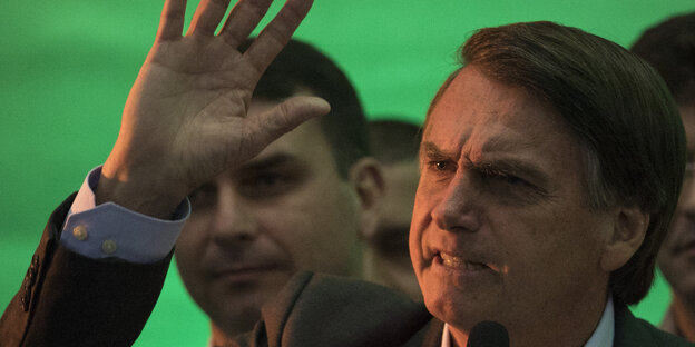 Vor einem grünen Bühnenhintergrund winkt Jair Bolsonaro in die Menge Vor einem grünen Bühnenhintergrund winkt Jair Bolsonaro in die Menge