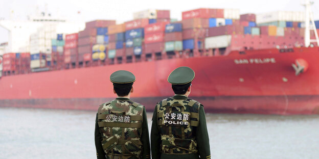 Zwei Polizisten stehen vor einem riesigen Containerschiff Zwei Polizisten stehen vor einem riesigen Containerschiff