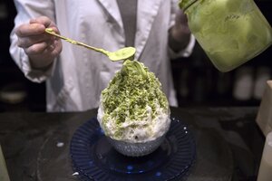 Mit einem Löffel wird grüne Sauce auf weißen Eiskristallen in einem Becher drapiert Mit einem Löffel wird grüne Sauce auf weißen Eiskristallen in einem Becher drapiert