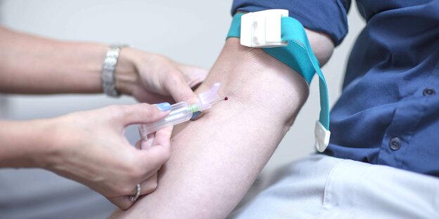 Die Hände einer Krankenschwester stechen eine Spritze in den Unterarm eines Patienten mit aufgekrempeltem Ärmel Die Hände einer Krankenschwester stechen eine Spritze in den Unterarm eines Patienten mit aufgekrempeltem Ärmel