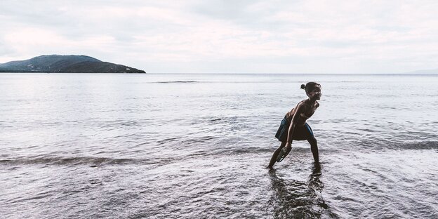 Eine junge Frau läuft an der Wasserkante zum See, im Hintergrund eine Insel Eine junge Frau läuft an der Wasserkante zum See, im Hintergrund eine Insel