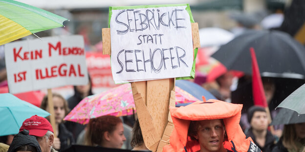 Demonstranten halten ein Schild mit der Aufschrift „Seebrücke statt Seehofer“ in die Höhe Demonstranten halten ein Schild mit der Aufschrift „Seebrücke statt Seehofer“ in die Höhe