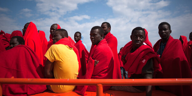 Auf einem Rettungsboot sitzen in Decken gehüllte Flüchtlinge Auf einem Rettungsboot sitzen in Decken gehüllte Flüchtlinge