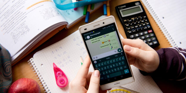 Eine Schülerin sitzt mit ihrem Handy und ihren Schulsachen an einem Schreibtisch Eine Schülerin sitzt mit ihrem Handy und ihren Schulsachen an einem Schreibtisch