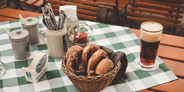 Ein Tisch mit einem Brotkorb mit Brezeln. Daneben ein Glas Bier