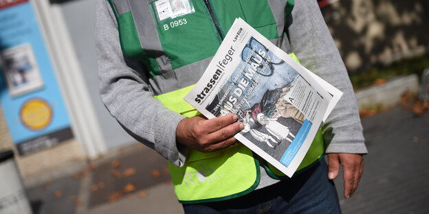 Zeitung Straßenfeger, gehalten von einer Person mit Warnweste hält Zeitung Straßenfeger, gehalten von einer Person mit Warnweste hält