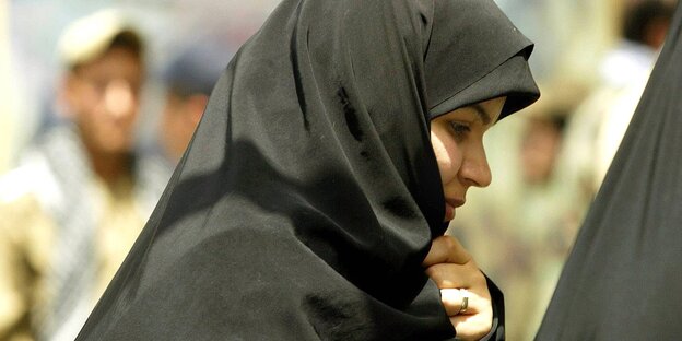 Eine iranische Frau mit Hijab. Unscharf im Hintergrund ein Mann, der in ihre Richtung schaut Eine iranische Frau mit Hijab. Unscharf im Hintergrund ein Mann, der in ihre Richtung schaut