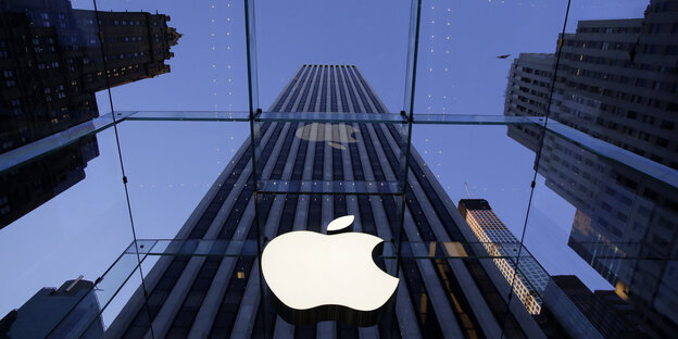 Ein angebissener Apfel, das Sysmbol des US-Konzerns Apple, hängt an einem Fenster. Im Hintergrund ist ein Wolkenkrazer zu sehen. Ein angebissener Apfel, das Sysmbol des US-Konzerns Apple, hängt an einem Fenster. Im Hintergrund ist ein Wolkenkrazer zu sehen.