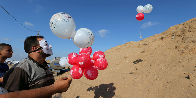 Zwei junge Palästinenser, von denen einer eine weiße Maske vor dem Gesicht trägt, halten mit Helium gefüllte Ballons, die sie mit Brandsätzen bestückt über die Grenze nach Israel schicken Zwei junge Palästinenser, von denen einer eine weiße Maske vor dem Gesicht trägt, halten mit Helium gefüllte Ballons, die sie mit Brandsätzen bestückt über die Grenze nach Israel schicken