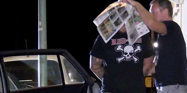 Ein Mann mit tätowierten Armen und Beinen, sein Gesicht unter einer Zeitung verdeckt Ein Mann mit tätowierten Armen und Beinen, sein Gesicht unter einer Zeitung verdeckt
