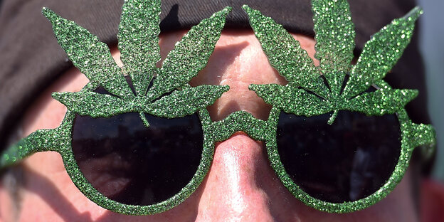Mann mit Sonnenbrille, deren Umfassung mit zwei Marihuanablättern verziert ist Mann mit Sonnenbrille, deren Umfassung mit zwei Marihuanablättern verziert ist