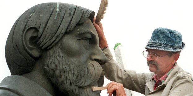 Die Zähne einer Bronzeplastik von Friedrich Engels werden von einem Mann gepflegt Die Zähne einer Bronzeplastik von Friedrich Engels werden von einem Mann gepflegt