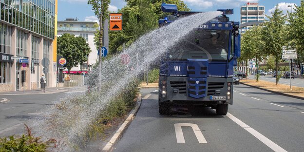 Ein Wasserwerfer der Polizei bespritzt den Grünstreifen einer Straße mit Wasser Ein Wasserwerfer der Polizei bespritzt den Grünstreifen einer Straße mit Wasser