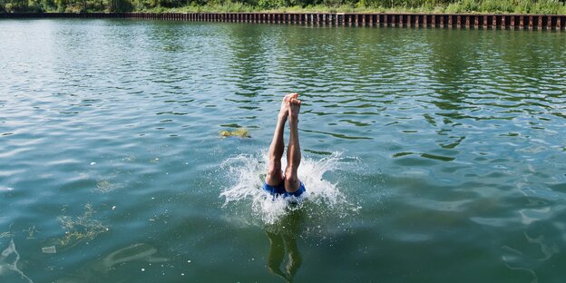 Die Beine eines Mannes ragen aus dem Wasser, in das er gerade mit einem Kopfsprung eingetaucht ist Die Beine eines Mannes ragen aus dem Wasser, in das er gerade mit einem Kopfsprung eingetaucht ist