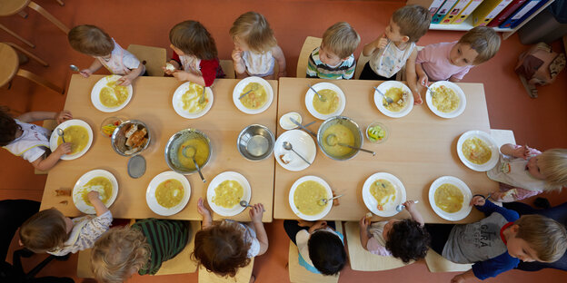 Kinder sitzen in einer Kita an einem Tisch und essen Suppe. Kinder sitzen in einer Kita an einem Tisch und essen Suppe.