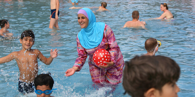 Eine Frau im Burkini spielt im Wasser mit Kindern. Eine Frau im Burkini spielt im Wasser mit Kindern.