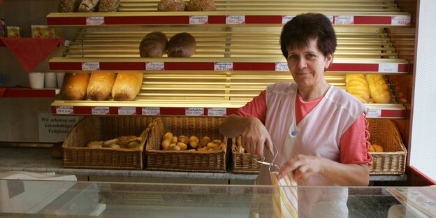 Eine Bäckereiverkäuferin steht hinter der Verkaufstheke und hält eine Tüte in der Hand Eine Bäckereiverkäuferin steht hinter der Verkaufstheke und hält eine Tüte in der Hand