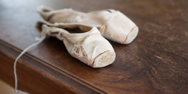 weiße Ballettschuhe liegen auf einem dunklen Holztisch weiße Ballettschuhe liegen auf einem dunklen Holztisch