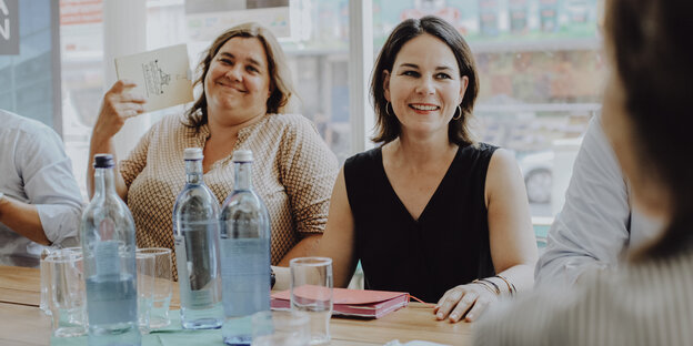 Annalena Baerbock sitzt am Tisch neben einer anderen Frau und lacht Annalena Baerbock sitzt am Tisch neben einer anderen Frau und lacht