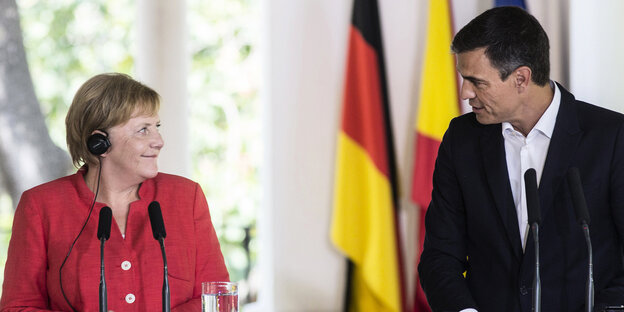 Merkel und Sánchez stehen vor Mikrofonen und gucken sich an Merkel und Sánchez stehen vor Mikrofonen und gucken sich an